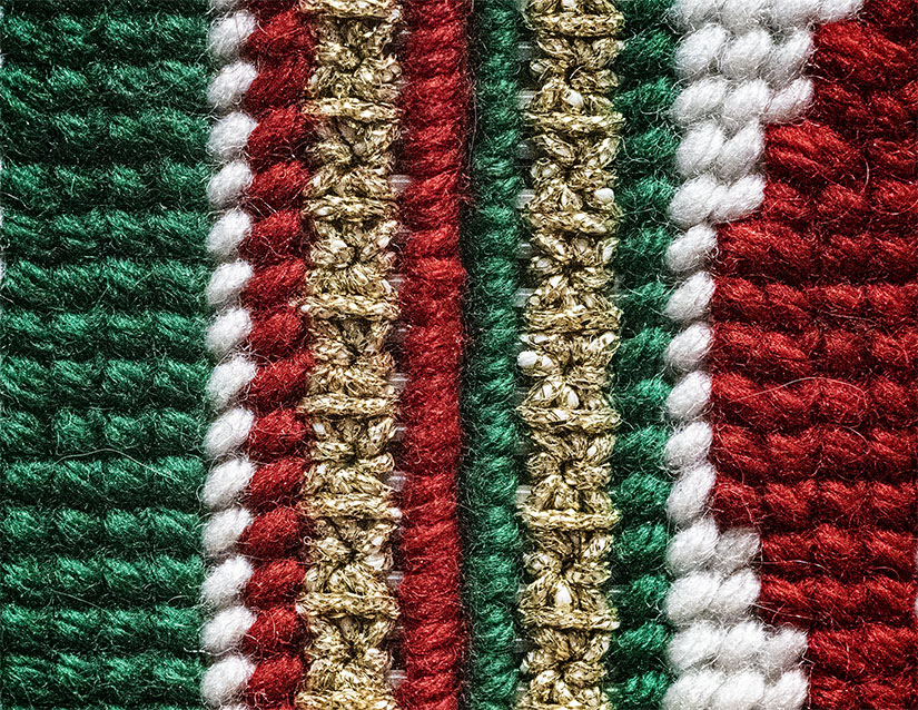 Close-up macro photograph of woven red, green, white, and gold threads, showing texture and precise craftsmanship